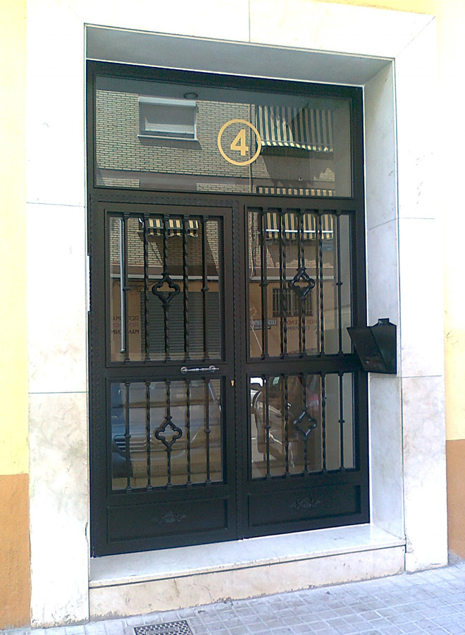 Puerta de una hoja abatible con fijos laterales y superior. Con adornos de fundición y cristal transparente.