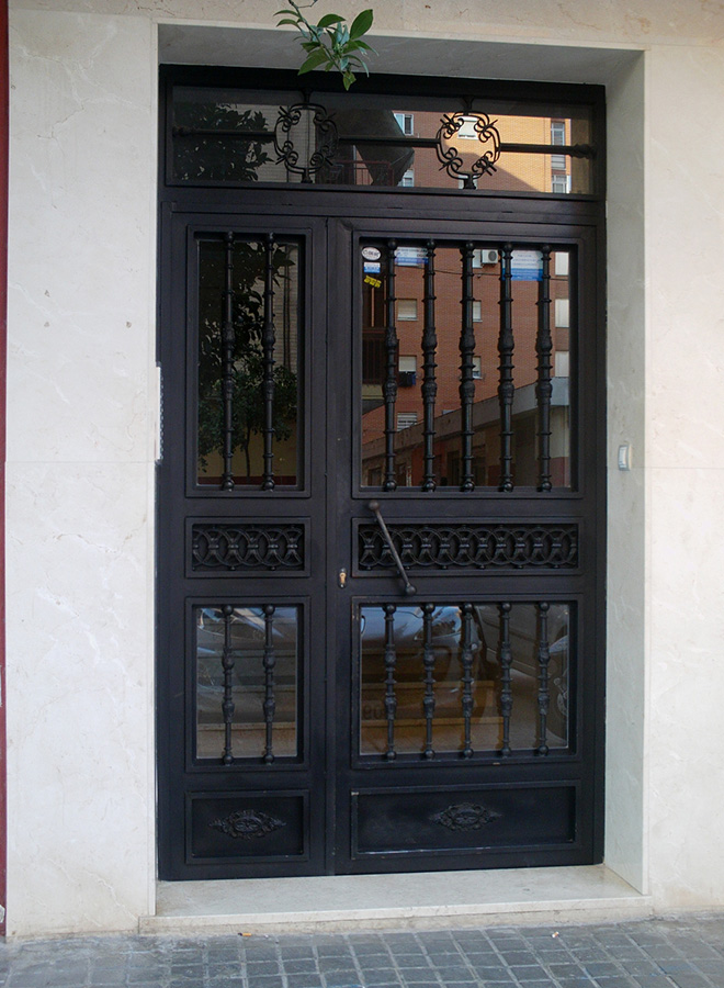 Puerta de una hoja abatible con fijos laterales y superior. Con adornos de fundición y cristal espejo.