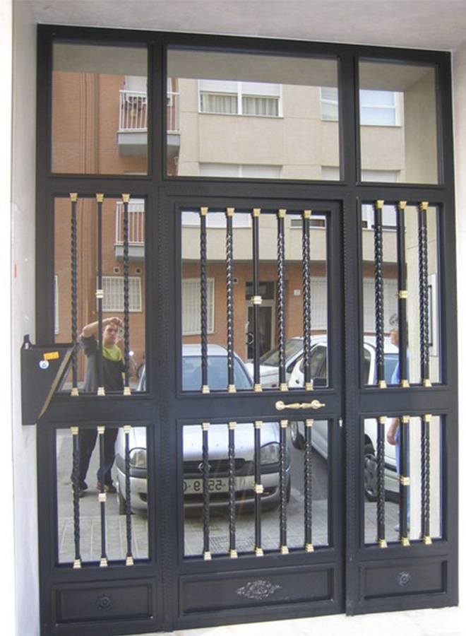 Puerta de una hoja abatible con fijos laterales y superior. Con adornos de bronce y cristal espejo.