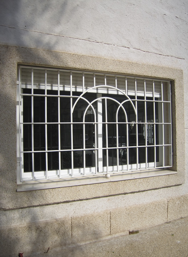 Reja de Bonrepos fija con diseño curvo en la parte superior, fabricada con barrotes de hierro macizo y pintada en color blanco. Colocada a medida en ventana exterior.